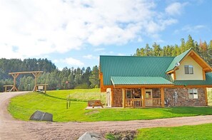 A lodge with a green roof, stone walls, and a wooden porch. - Cottage at Storm Mountain #5 (Hill City)