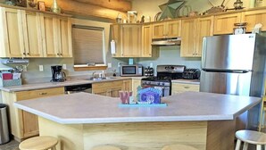 A kitchen with wooden cabinets, a central island with stools, a refrigerator, and a stove. - Cottage at Storm Mountain #5 (Hill City)