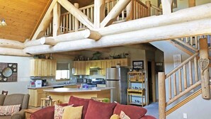 A spacious living area with a red sofa, wooden staircase, and a kitchen with modern appliances. - Cottage at Storm Mountain #5 (Hill City)