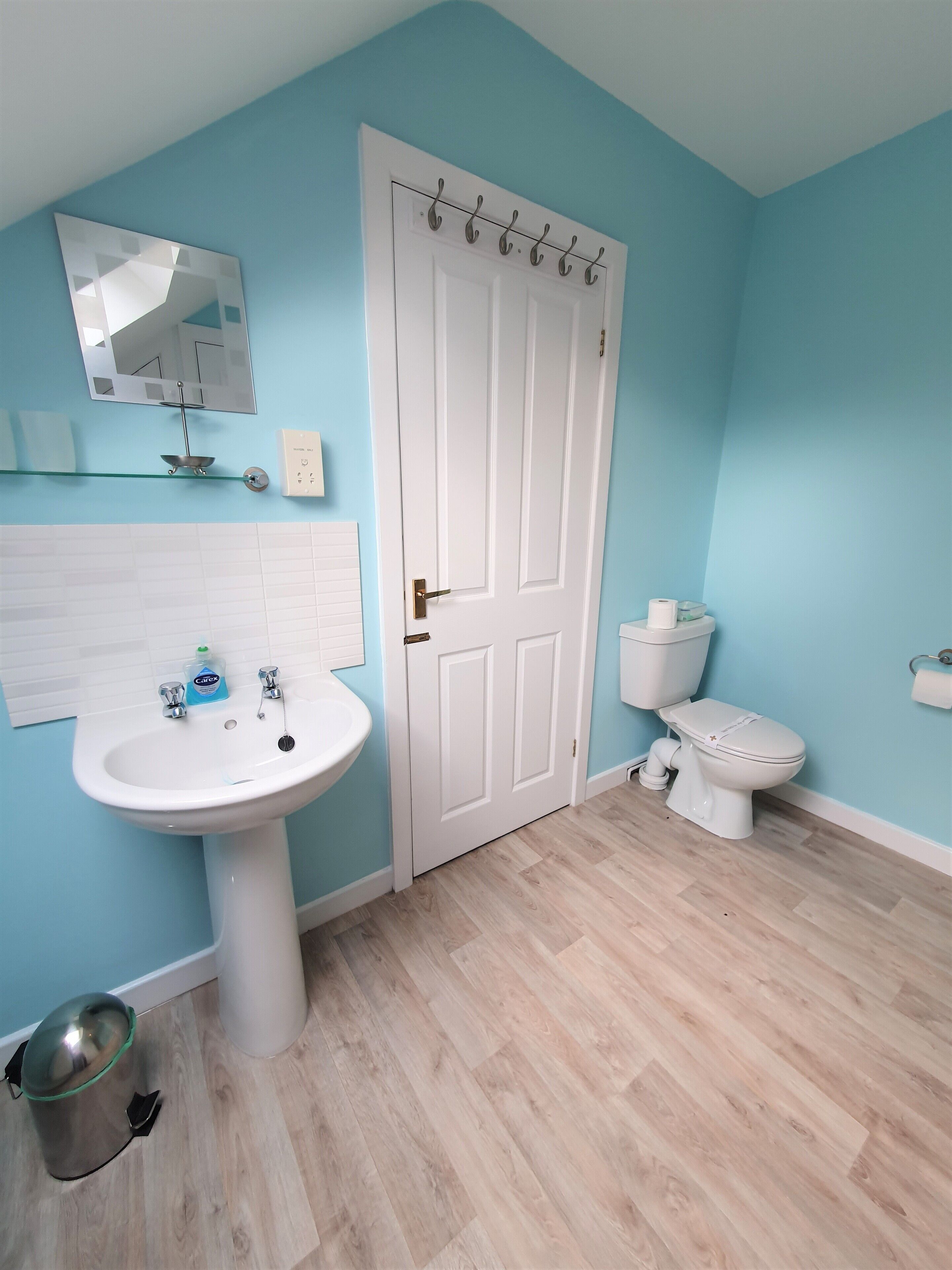 Une salle de bain avec un lavabo blanc, des toilettes et une porte surmontée d’un miroir.