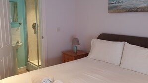 Quarto de hotel com cama, um quadro na parede, mesa de cabeceira e banheiro visível através de uma porta aberta.