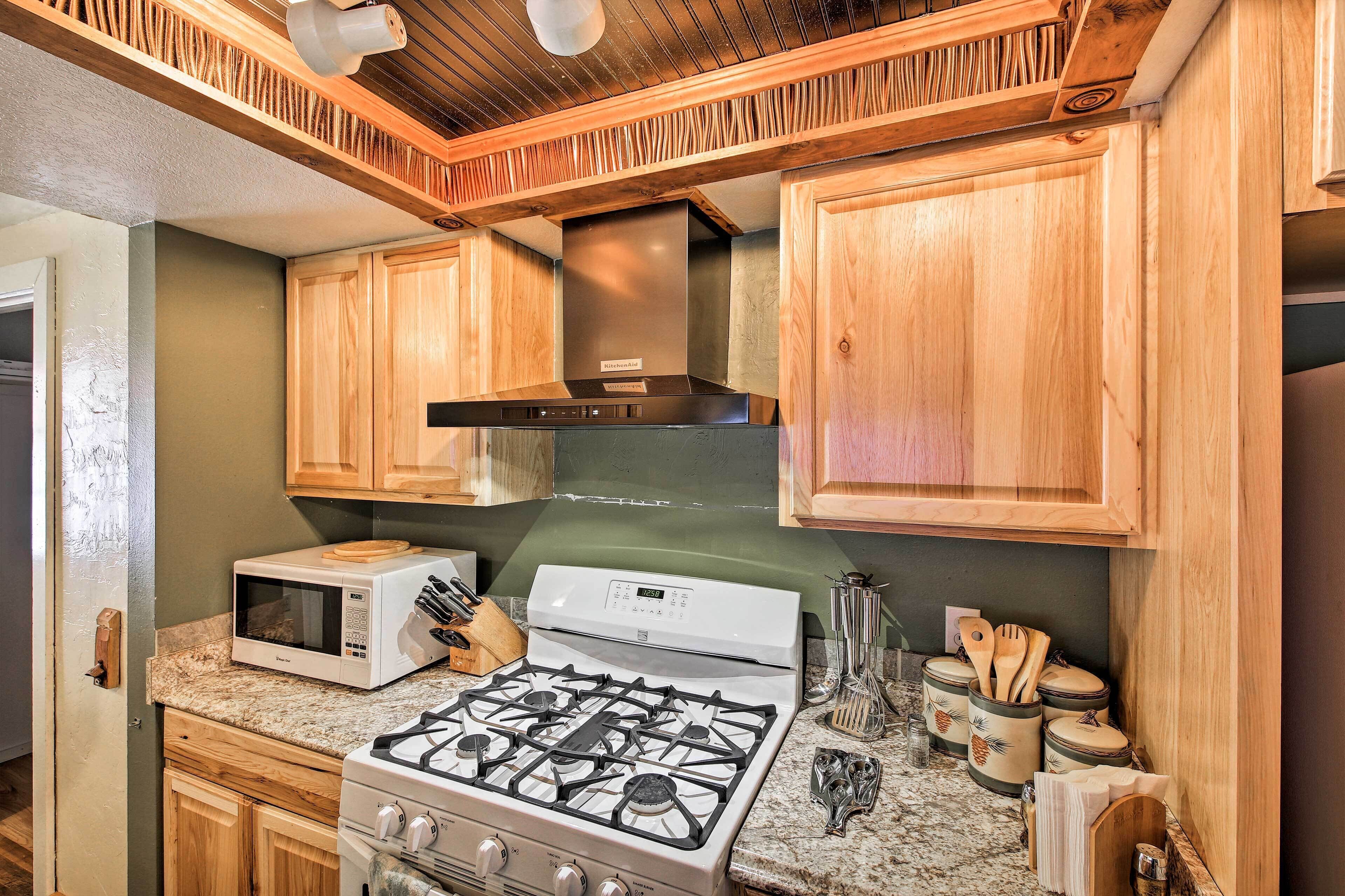 A kitchen with wooden cabinets, a microwave, a stove, and various utensils.