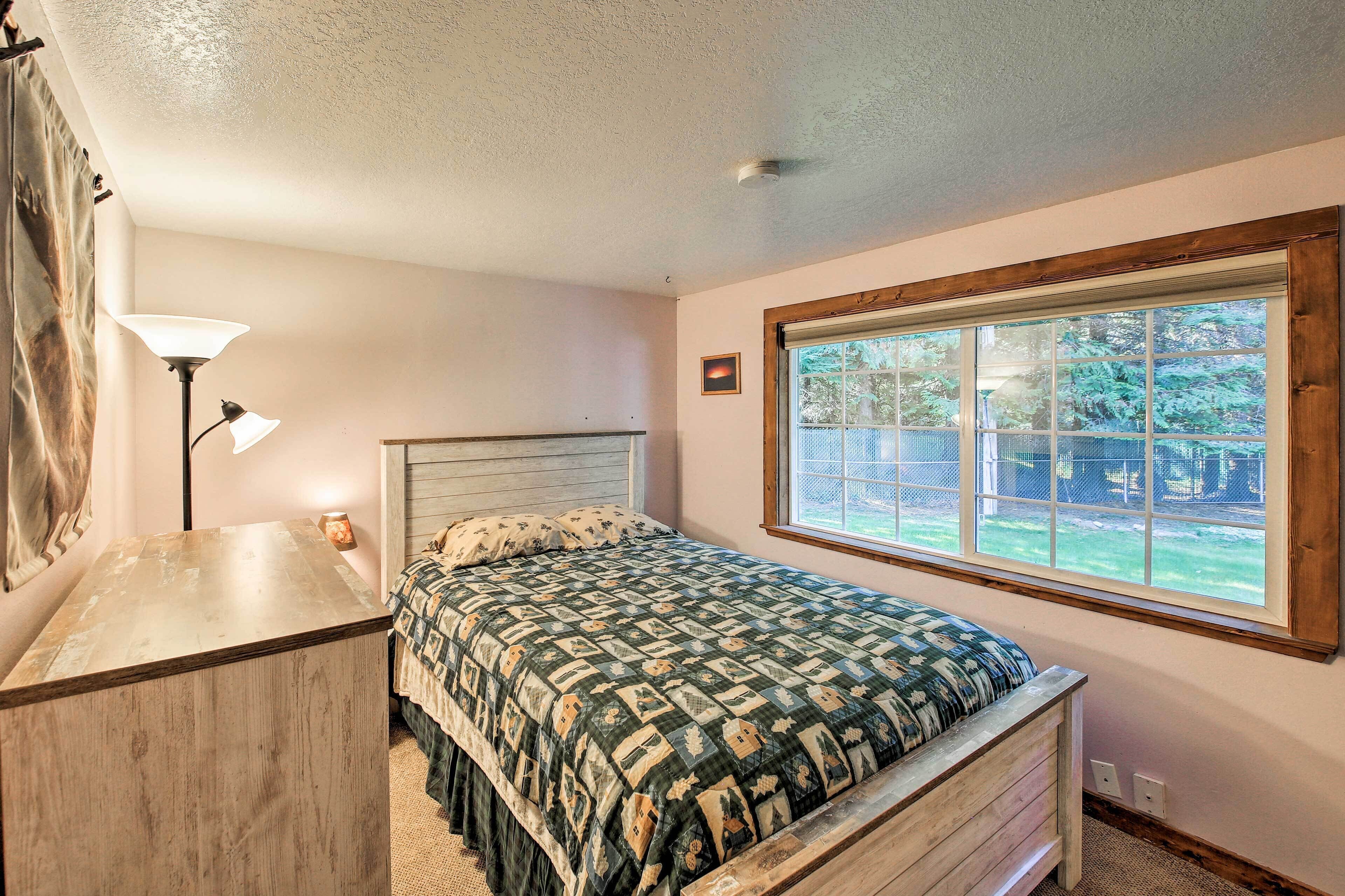 A bedroom with a bed, a desk, a lamp, and a window with a view of the outdoors.