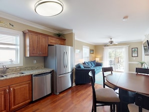 A kitchen with wooden cabinets, stainless steel appliances, and a dining area with a table and chairs. - Heated Pool Access | 5*Clean | Flex Cancelation (Tybee Island)
