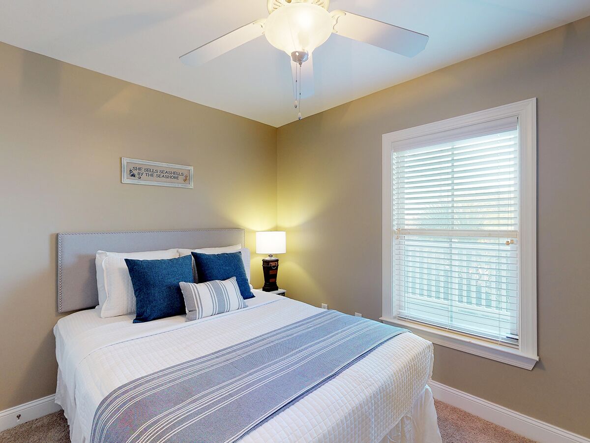 A bedroom with a bed, a nightstand, a ceiling fan, and a window with blinds.