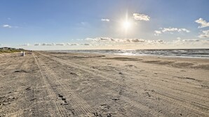 Una spiaggia sabbiosa con impronte e solchi di pneumatici, che conduce verso l'oceano sotto un cielo sereno con il sole splendente.