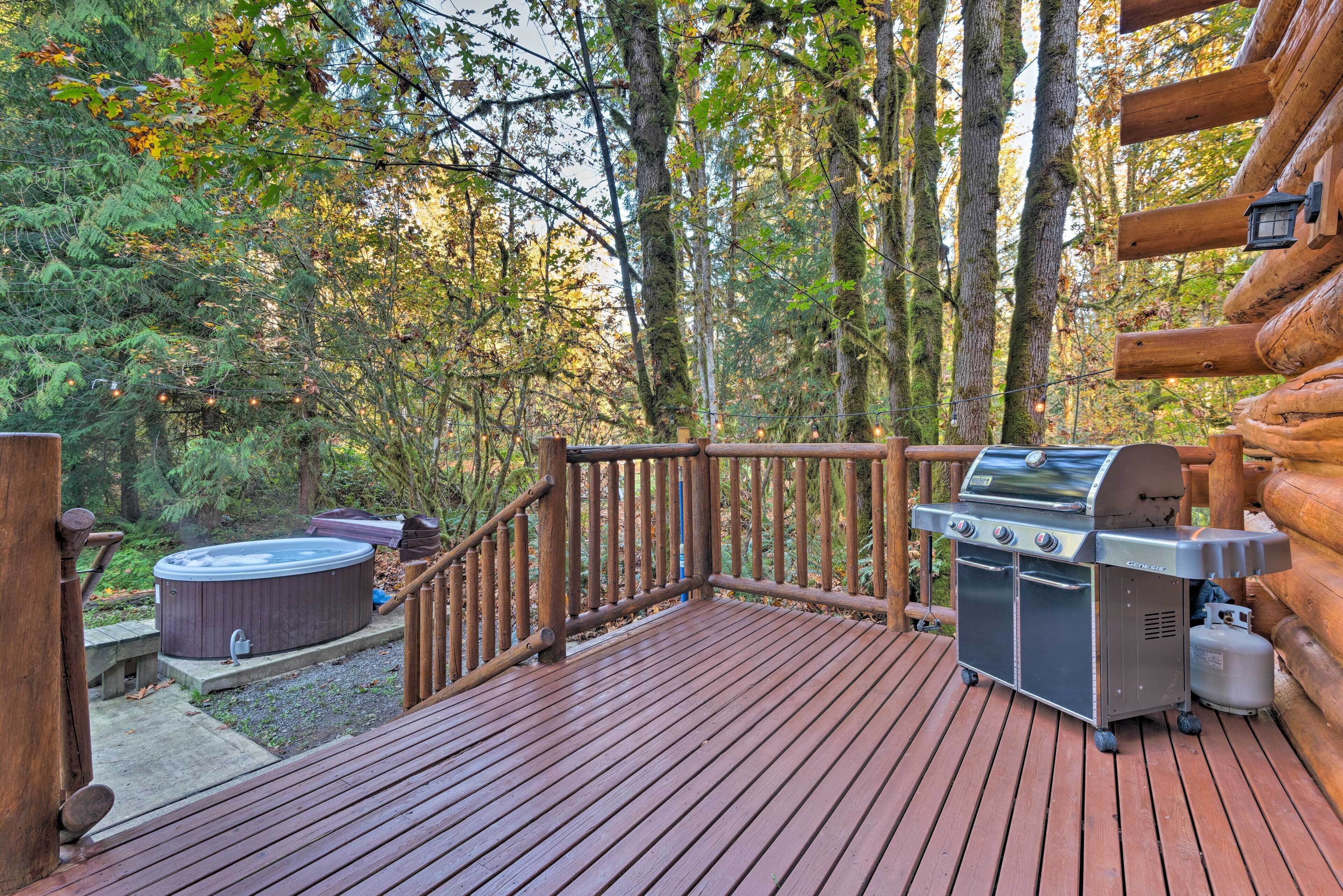 Una terrazza in legno con barbecue e vasca idromassaggio, immersa nel verde.
