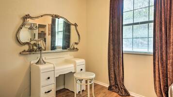 A room with a vanity, a mirror, a stool, and a window with curtains.