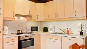 A compact kitchen with light-colored cabinets, a microwave, a coffee maker, and a sink.