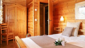 A wooden cabin room with a bed, a chair, a nightstand, and a wall-mounted lamp.