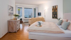 A bedroom with a bed, a dresser, a chair, a TV, and a window with a view of mountains. - Cosy apartment for 2 guests with WIFI, TV, balcony and pets allowed (Ascona)