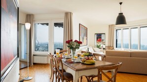 A dining area with a wooden table, chairs, and a view of the city through large windows. - Nice apartment for 4 people with WIFI, TV, balcony and pets allowed (Ascona)