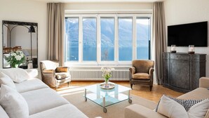 A modern living room with a large window, a flat-screen TV, and a cozy seating area. - Nice apartment for 4 people with WIFI, TV, balcony and pets allowed (Ascona)