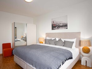 A modern bedroom with a large bed, a wardrobe, a chair, and a painting on the wall.