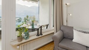 A living room with a view of a lake and mountains, a sofa, a table with candles, and a lamp.