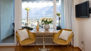 A room with a table set for two, a view of a mountainous landscape, and a television mounted on the wall. - Beautiful apartment for 2 people with WIFI, TV, balcony and pets allowed (Ascona)