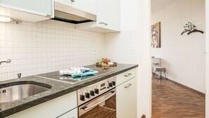 A compact kitchen with white cabinets, a stainless steel sink, a built-in oven, and a countertop with a toaster and a bowl of fruit. - Beautiful apartment for 2 people with WIFI, TV, balcony and pets allowed (Ascona)
