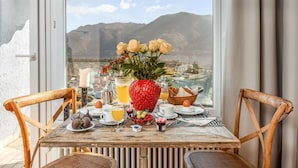 A breakfast table with a view of mountains and a city, featuring a vase of flowers, a strawberry, and various breakfast items. - Lovely apartment for 2 people with WIFI, TV, balcony and pets allowed (Ascona)