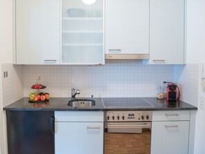 A kitchen with white cabinets, a stainless steel sink, a dishwasher, and a red electric kettle.