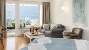 A hotel room with a bed, a sofa, a chair, a table with flowers, and a view of the mountains.