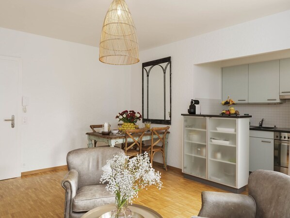 A modern living room with a sofa, a dining table with chairs, a kitchen area with cabinets and a stove, and a hanging light fixture. - Lovely apartment for 4 people with WIFI, TV, balcony and pets allowed (Ascona)