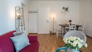 A living room with a red sofa, a dining table with chairs, a vase of white flowers, and a floor lamp. - Lovely apartment for 4 guests with WIFI, TV, balcony and pets allowed (Ascona)