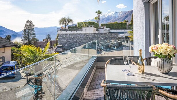 A balcony with a glass railing overlooking a mountainous landscape and a body of water.