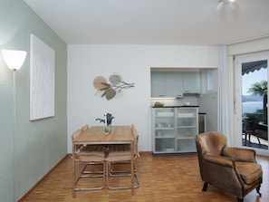 A dining area with a wooden table and chairs, a kitchen with white cabinets, and a view of the outdoors through a sliding glass door.