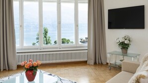 A modern living room with a large window, a flat-screen TV, a glass coffee table with flowers, and a sofa. - Nice apartment for 4 people with WIFI, TV, balcony and pets allowed (Ascona)