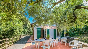 An outdoor patio with white furniture, a table with a bowl of fruit, and a green door. - Stunning private villa for 7 guests with private pool, TV, terrace and pets allowed (Rosignano Solvay-castiglioncello)
