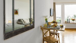A room with a large mirror, a dining table with breakfast items, a sofa, and a window with a view. - Lovely apartment for 2 people with WIFI, TV, balcony and pets allowed (Ascona)