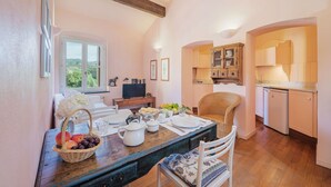 Zona pranzo con tavolo di legno apparecchiato per un pasto, una sedia in vimini e vista sulla cucina.