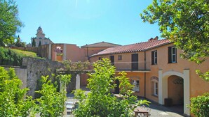 Un cortile con un muro in pietra, una piccola fontana e un edificio con tetto in tegole rosse.