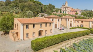 Una villa su una collina con diversi edifici, un campanile ben visibile e una strada privata che conduce a un'auto parcheggiata.