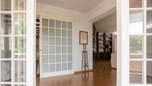 Un corridoio con pavimento in legno, una porta bianca con pannelli di vetro smerigliato e una libreria piena di libri e oggetti decorativi.