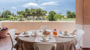 Un balcone con un tavolo apparecchiato per la colazione, con vista su una zona residenziale alberata e auto parcheggiate.