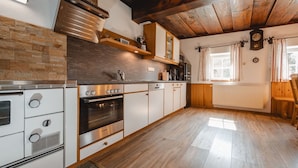 A kitchen with a stove, oven, and microwave, wooden cabinets, and a window with curtains.