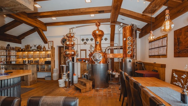 A rustic interior with exposed wooden beams, a bar area with various bottles, and a seating area with leather chairs.