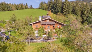 A traditional wooden house with a balcony, surrounded by lush greenery and trees.