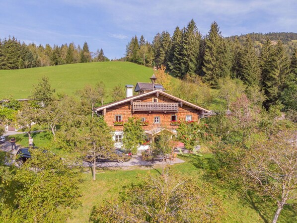 A traditional wooden house with a balcony, surrounded by lush greenery and trees.
