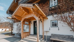 A wooden building with a covered entrance, a bench, and a sign indicating it's a home.