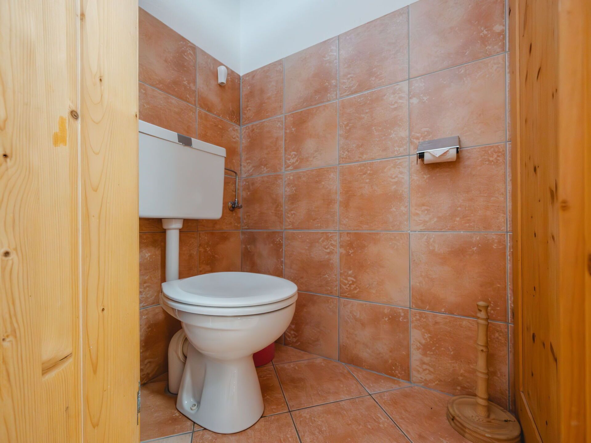 A small bathroom with a white toilet, a wooden door, and orange-tiled walls.