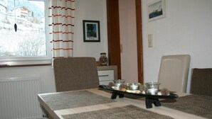 Un'area pranzo con un tavolo apparecchiato per due, un termosifone, una finestra con tende e un quadro appeso al muro.