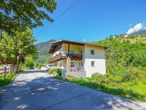 A two-story building with a balcony, a paved road in front, and a mountainous backdrop. - Beautiful apartment for 4 people with WIFI, TV, patio, pets allowed and panoramic view (Pians)