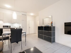 A modern kitchen with white cabinets, a dining area with a black table and chairs, and a black entertainment unit with a mirror and decorative items. - Lovely apartment for 2 guests with A/C, WIFI, TV and balcony (Interlaken)