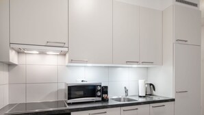 Een moderne keuken met witte kasten, een ingebouwde oven, een magnetron, een waterkoker en een spoelbak.