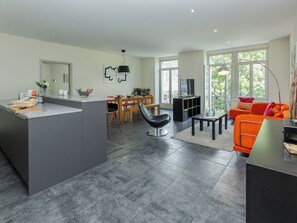 A modern kitchen with a central island, dining area with chairs, a sofa, and a TV.