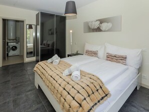 A modern bedroom with a large bed, a built-in washing machine, and a separate bathroom.