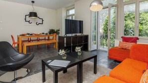 A modern living room with a dining area, a black leather chair, a red sofa, and a television on a dark stand. - Beautiful apartment for 4 people with WIFI, TV, balcony and panoramic view (Interlaken)