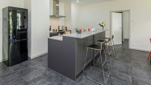 A modern kitchen with a central island, bar stools, a refrigerator, and a dining area with chairs. - Beautiful apartment for 4 people with WIFI, TV, balcony and panoramic view (Interlaken)